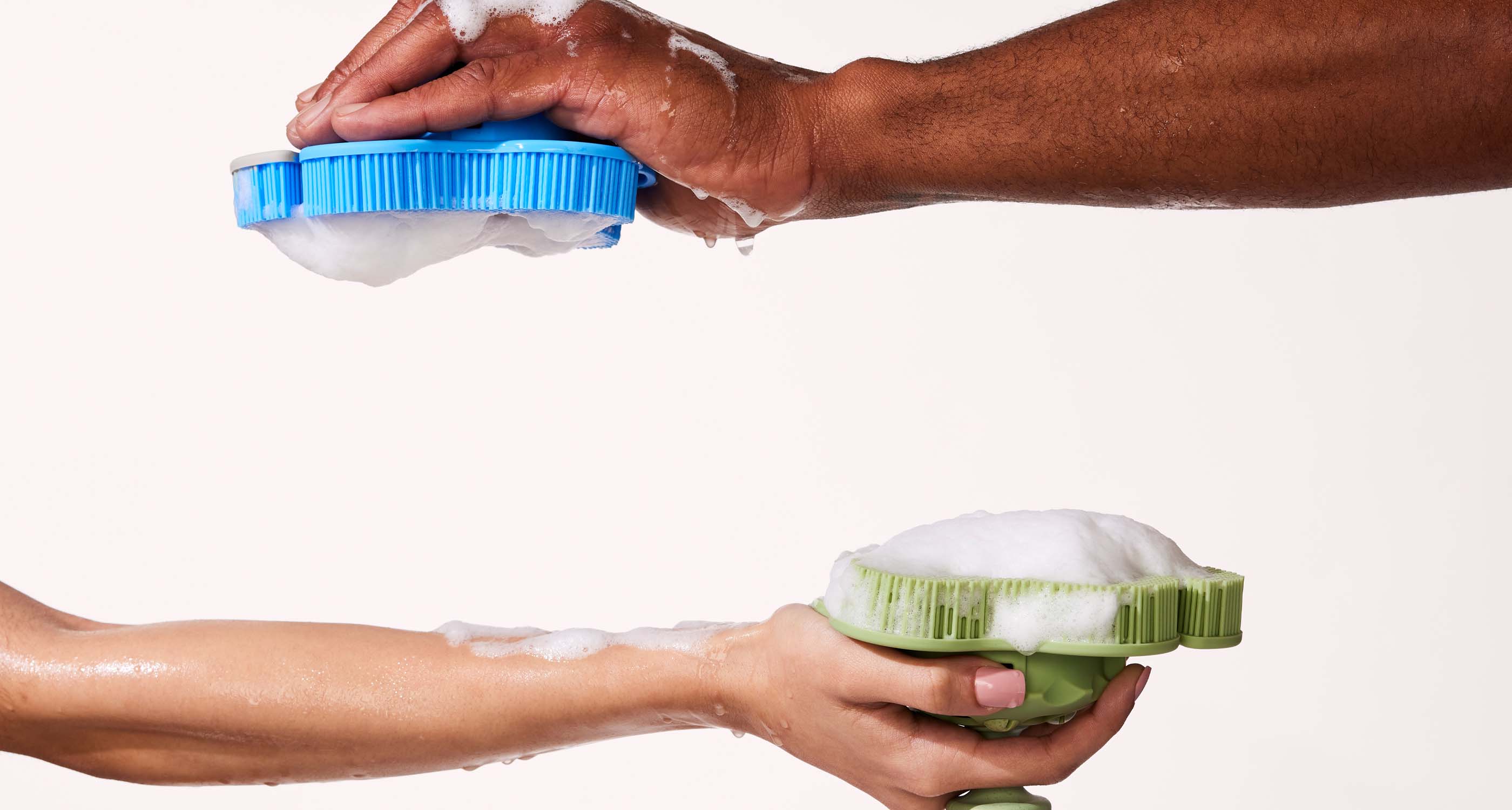 A man's arm and women's arm coming in from opposite sides of the image, holding a sudsy smoosh scrubber in hand