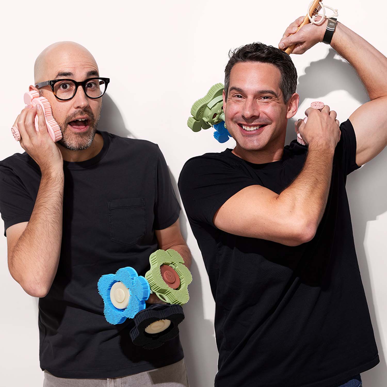 Founders Adam and Adam in black shirts, holding smoosh scrubbers in hand posing, happy