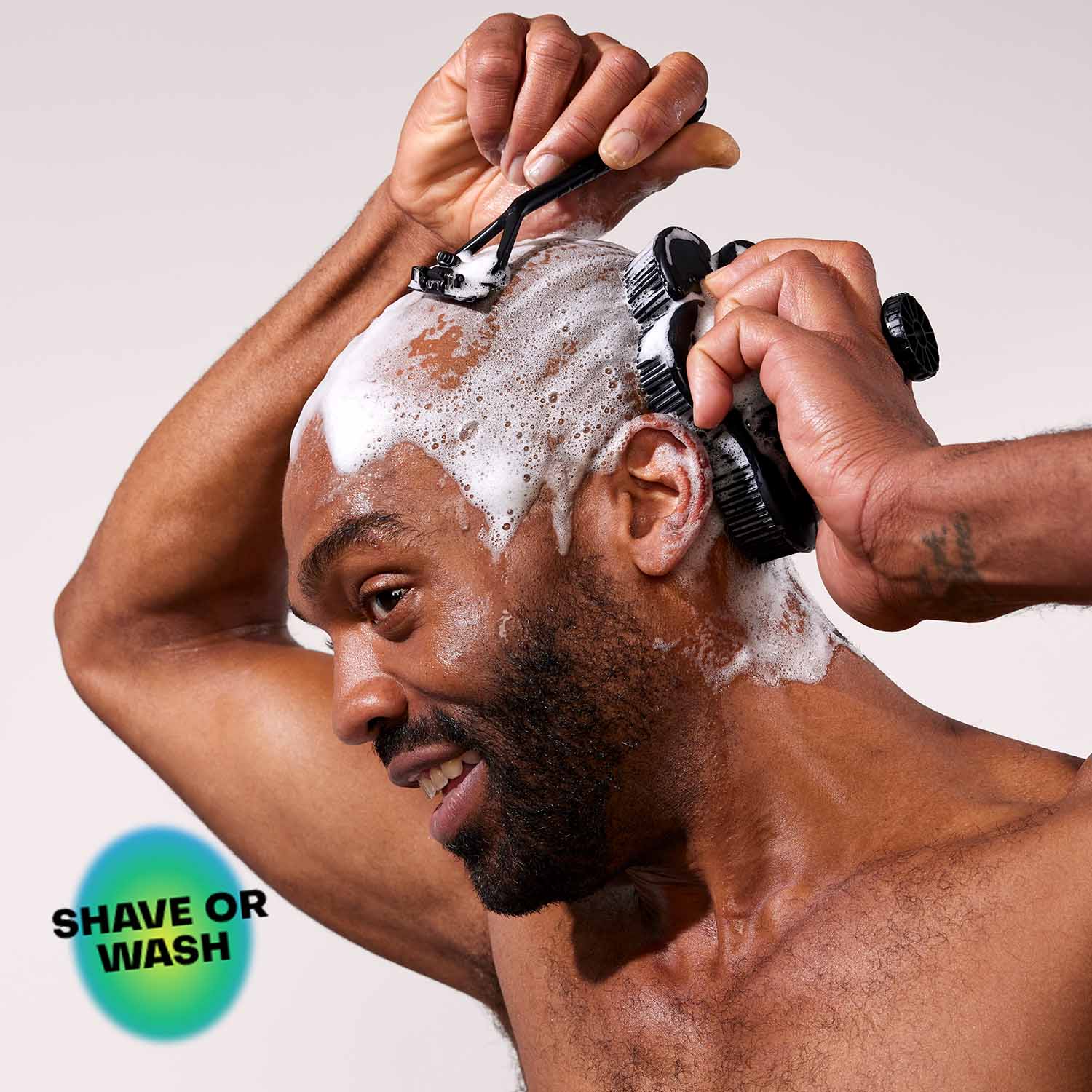 Man shaving his head with a Leaf Razor, and a smoosh scrubber in black in his other hand